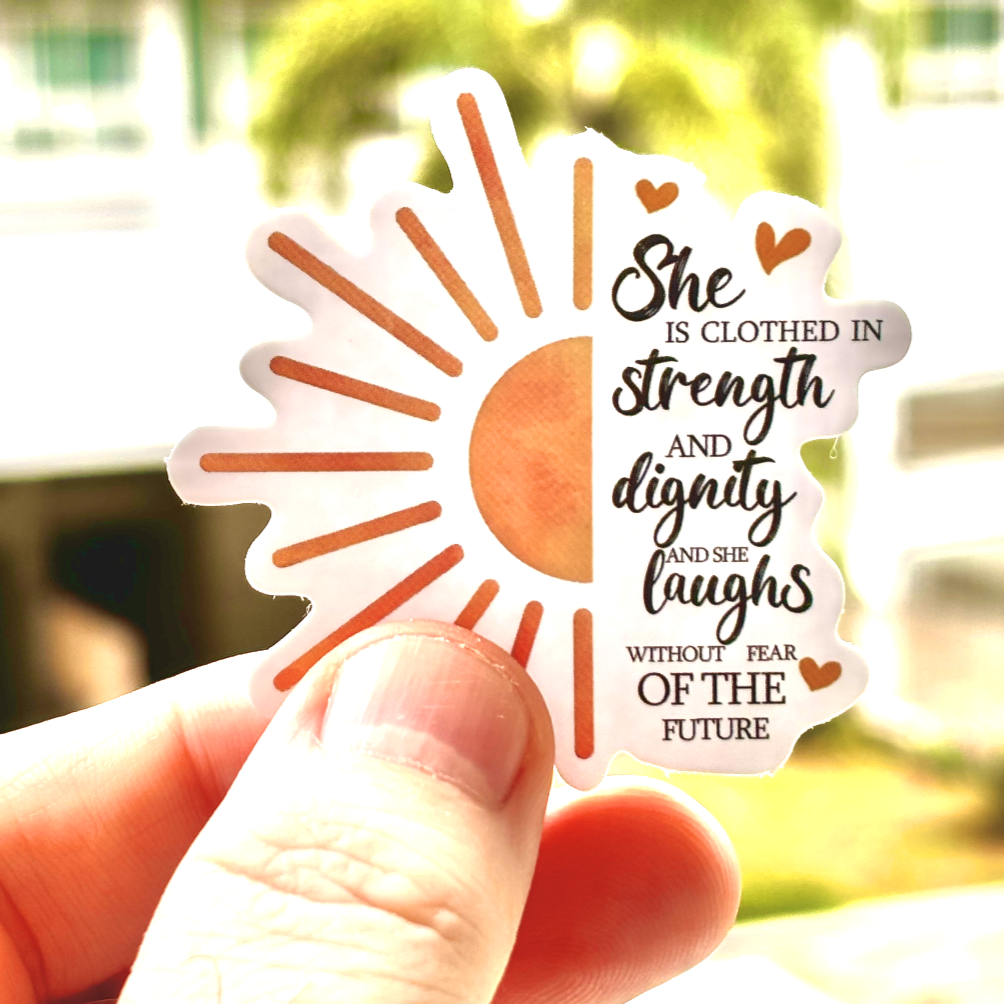 Inpsirational Sticker with the quote 'She is clothed in strength and dignity and she laughs without fear of the future. - Proverbs 31:25-31, flanked by the sun and hearts. Ideal for decorating planners, scrapbooks, and more, this sticker brings a message of faith and strength.