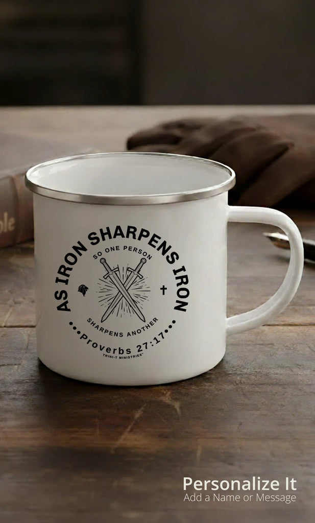White enamel Camping Mug with Iron Sharpens Iron Graphic sitting on a rugged desk with a leather Bible and leather gloves in the background.