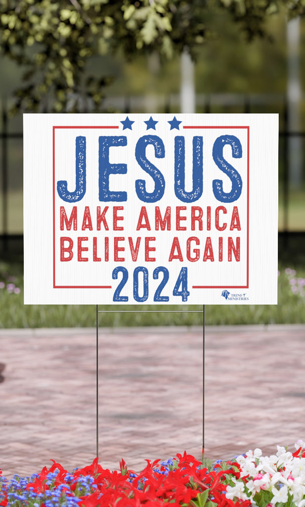 A Jesus 2024 - Make America Believe Again Yard Sign in a garden. Looking to make a statement that transcends politics and unites us all in faith? Introducing our Jesus 2024 yard sign, a playful yet powerful reminder that our true savior is in charge.  Emulating the familiar design of political signs that dot the American landscape during election season.