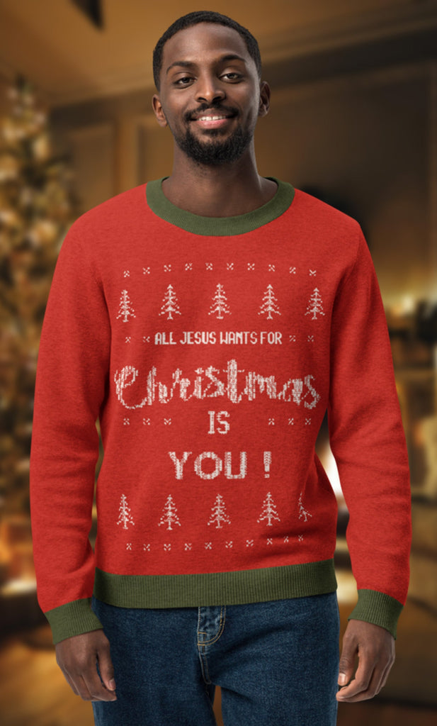 All Jesus Wants for Christmas Is You knitted ugly Christmas sweater, featuring festive red fabric with white text and Christmas tree designs, unisex holiday apparel for Christians. Perfect for Christmas parties, faith-based gatherings, and spreading festive cheer. Retro style ugly sweater with green ribbed collar, cuffs, and hem. Knitted sweater is modeled by an African American man in a cozy Christmas setting.