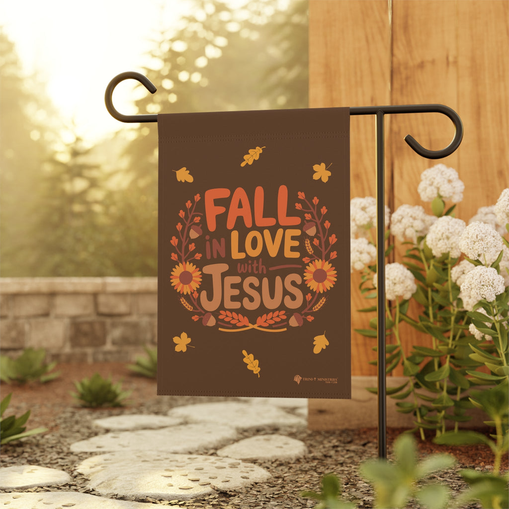 Close-up view of Fall in Love with Jesus garden flag hanging on a stake in a garden, Christian fall decor for outdoor display, 12x18 inches.