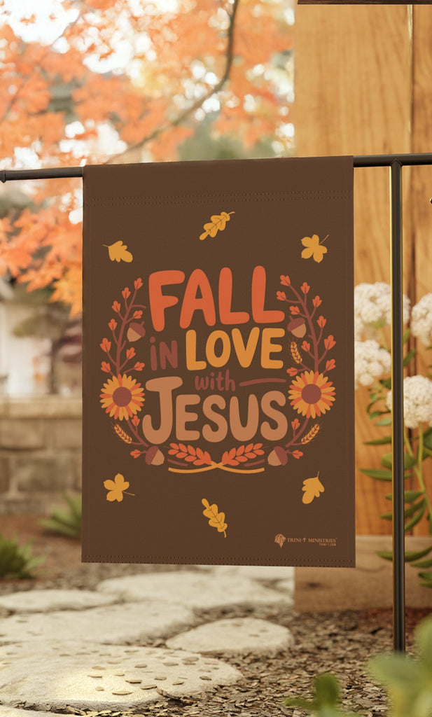 Fall in Love with Jesus garden flag hanging from a garden stake, surrounded by autumn decor, Christian fall-themed flag, 12x18 inches, double-sided.