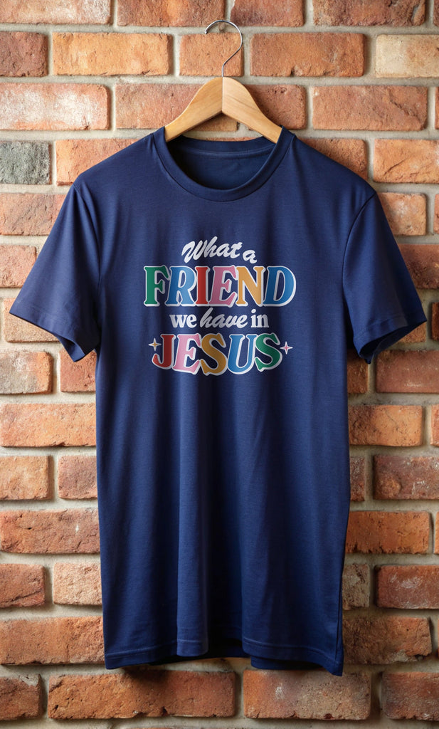 A navy blue Friend in Jesus - T-shirt hanging on a brick wall featuring vibrant, multi-colored text reading 'What a Friend we have in Jesus.' Available in various colors, these Christian-themed shirts are designed for men and women who want to proudly display their faith. Made from soft, breathable fabric, these t-shirts are perfect for everyday wear, church gatherings, or casual outings. The design, inspired by John 15:15, serves as a daily reminder that Jesus is 