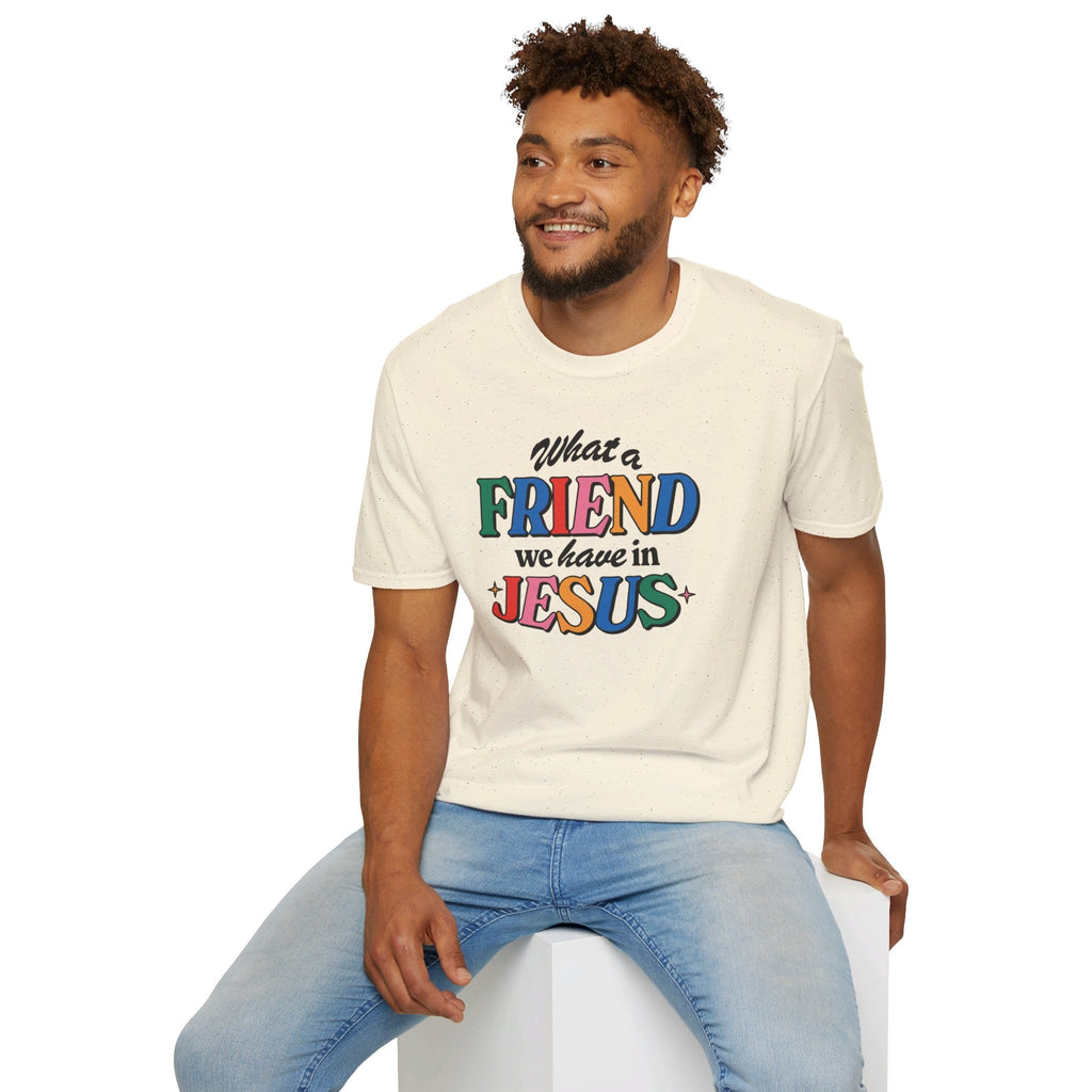 A seated man wearing a natural colored Friend in Jesus T-shirt.