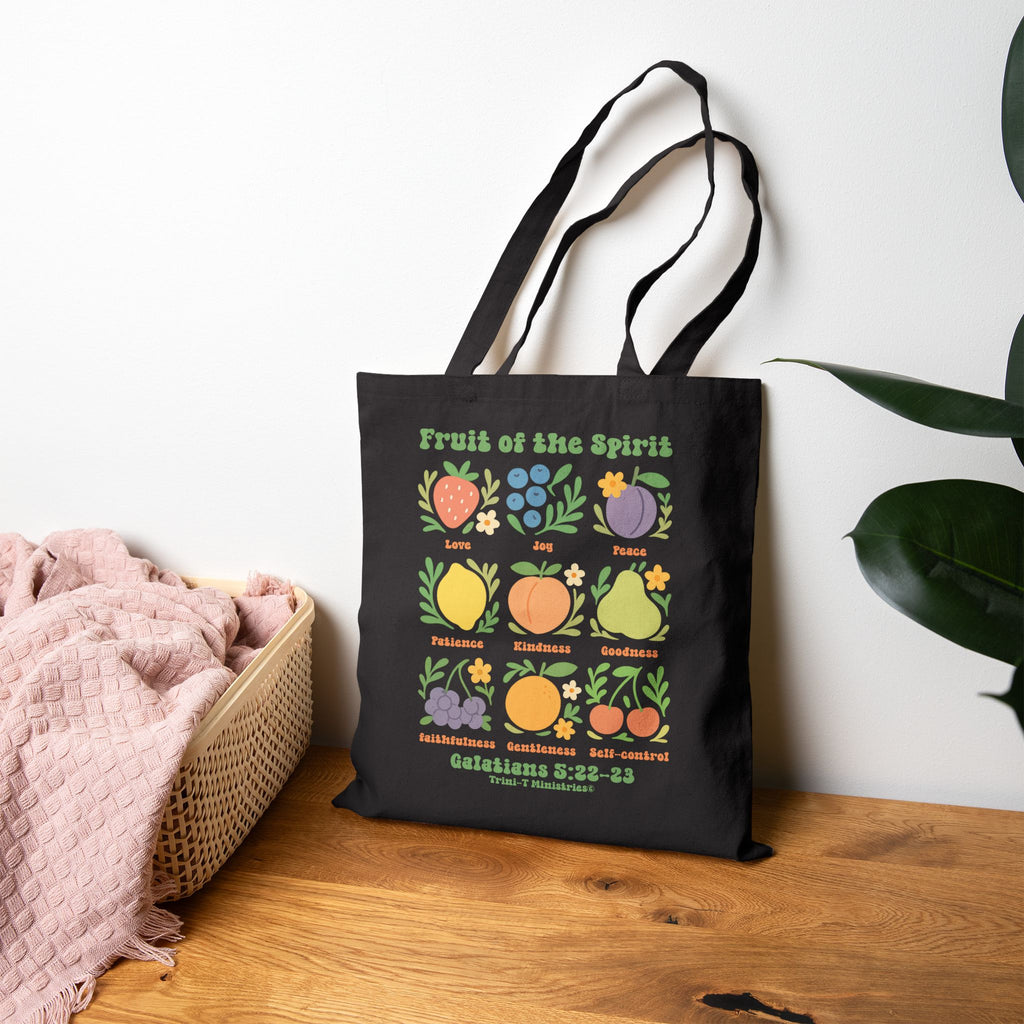 Black canvas Fruit of the Spirit Christian tote bag on wooden table, styled with plant.
