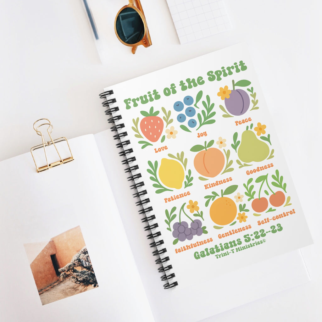 Flat lay of the Fruit of the Spirit Journal on a white desk with sunglasses, notepad, and photo card. Front cover features colorful fruit graphics and Galatians 5:22–23.