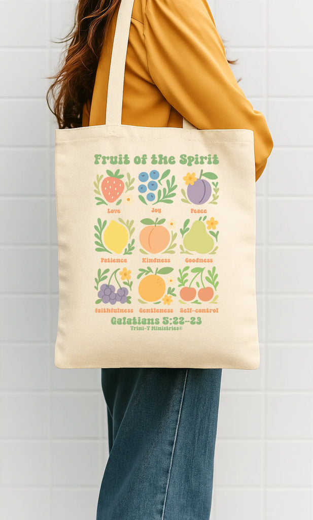 Woman holding a natural canvas tote bag featuring Fruit of the Spirit design from Galatians 5:22–23.