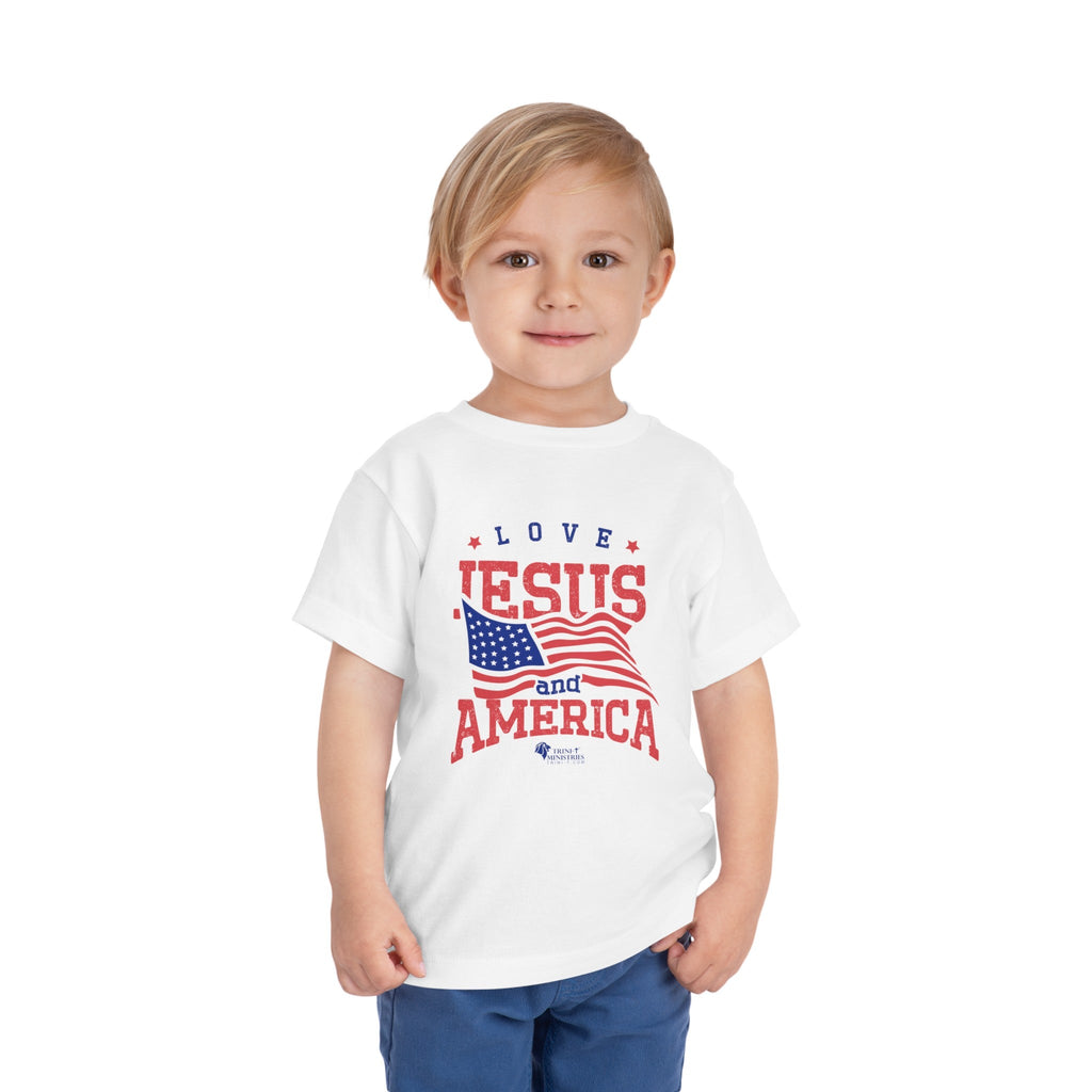 Young boy modelling a White Trini-T Ministries' Love Jesus and America Bella+Canvas 3001T shirt. Get our "Love Jesus and America" Toddler T-Shirt to let your toddler display their faith and patriotism. This delightful and motivating graphic tee is ideal for parents, relatives, and friends who wish to spread the Word of God and express their love for America through their toddler's clothing.