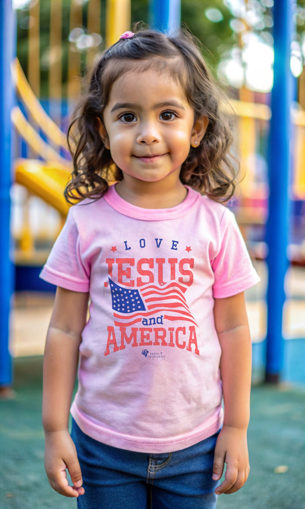 Little girl at the playground, wearing Pink Trini-T Ministries' Love Jesus and America Bella+Canvas 3001T shirt. Get our "Love Jesus and America" Toddler T-Shirt to let your toddler display their faith and patriotism. This delightful and motivating graphic tee is ideal for parents, relatives, and friends who wish to spread the Word of God and express their love for America through their toddler's clothing.