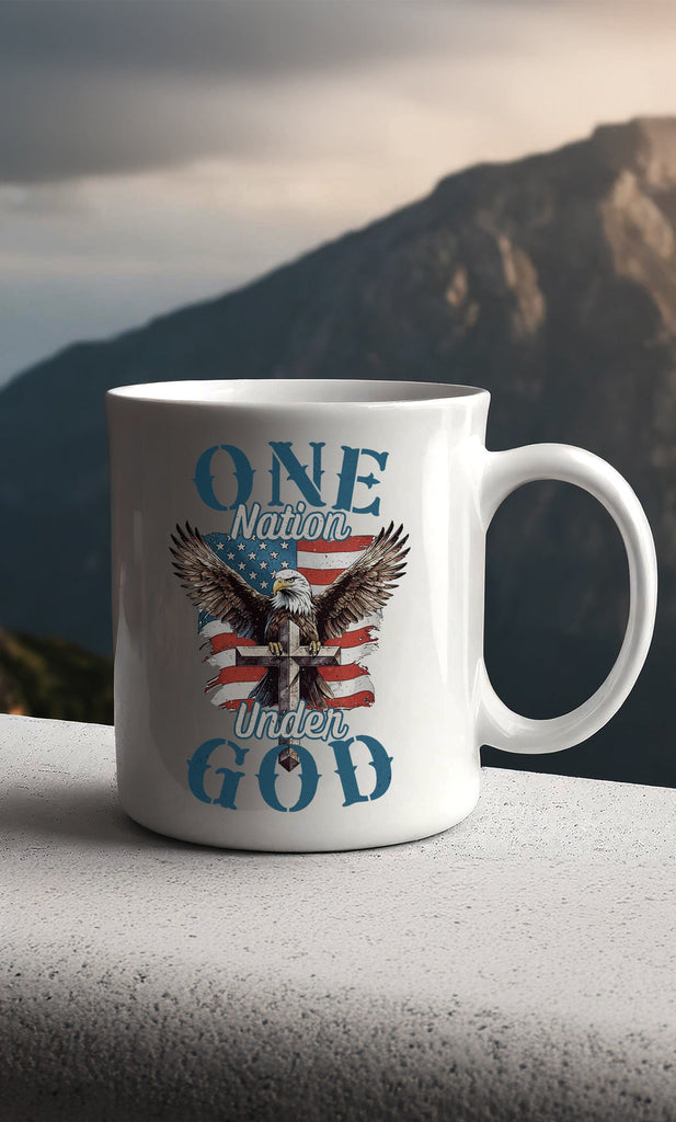 One Nation Under God - Eagle - Mug sitting in front of a rugged mountain at sunrise. Enjoy your favorite hot beverage with a touch of faith and patriotism using our "One Nation Under God" patriotic ceramic mug. This classic white mug is perfect for coffee, tea, and hot chocolate enthusiasts. It features a striking design with an American Bald Eagle, a Cross, and the iconic American flag.